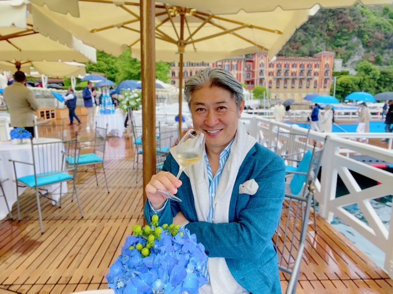 湖畔のテラスで青い紫陽花とグラスを手にする西田理一郎