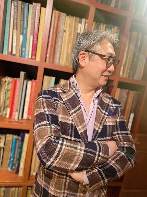 書棚の前でチェックのジャケットをまとう西田理一郎