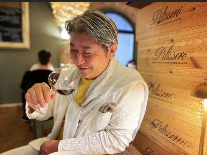 ワイン木箱の壁の前でテイスティングする西田理一郎