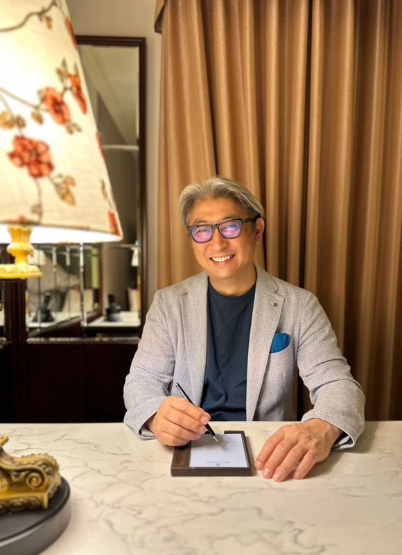 大理石のデスクで書きものをする西田理一郎