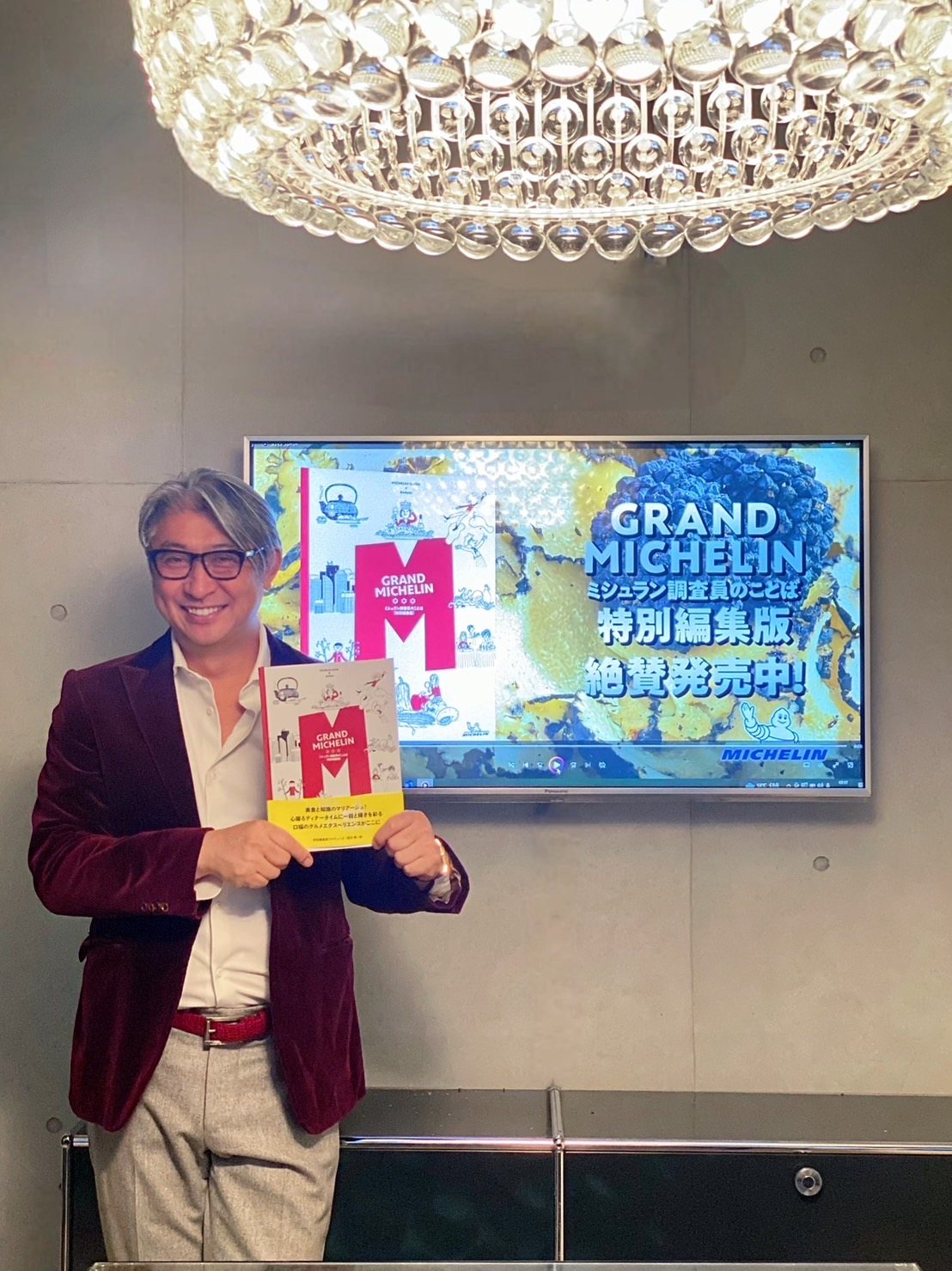『GRAND MICHELIN』を手に、発売告知の画面の前に立つ西田理一郎