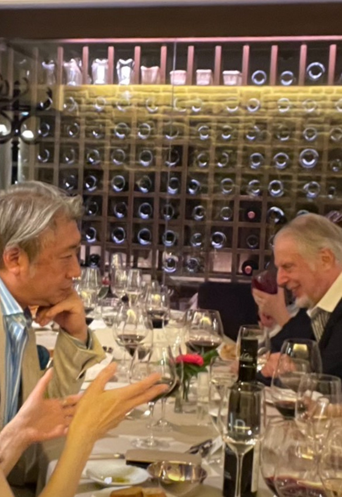 ワインセラーを背にした晩餐で、頬杖をついて向かいの客の話に耳を傾ける西田理一郎