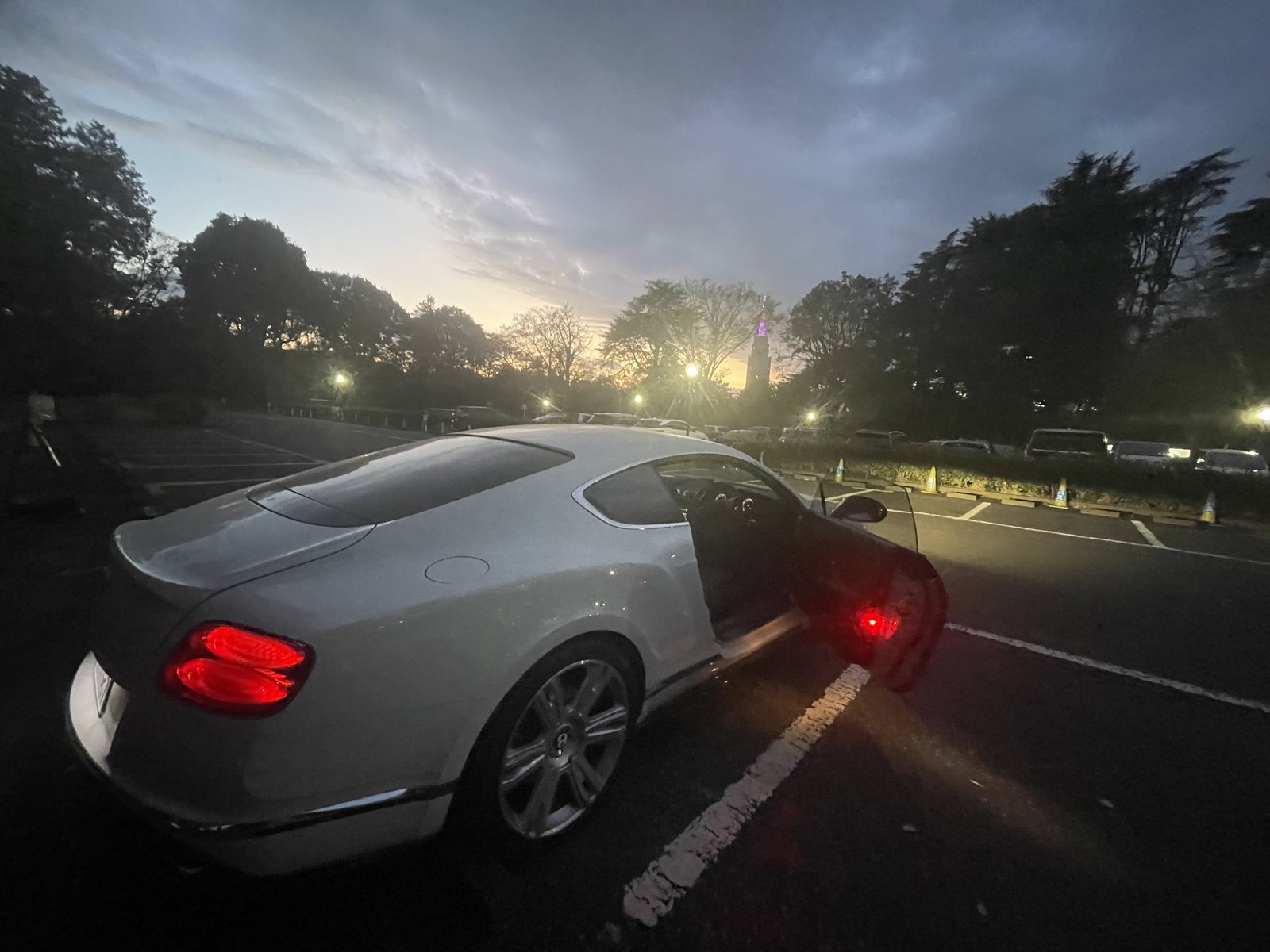 夕暮れの駐車場で、ドアを開けたままの白いベントレー